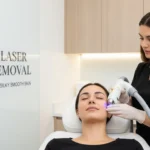 A professional laser hair removal specialist performing facial laser hair removal on a relaxed, smiling client in a modern clinic setting.